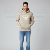 Man wearing a beige Emporio Armani hoodie and blue jeans on a gray background